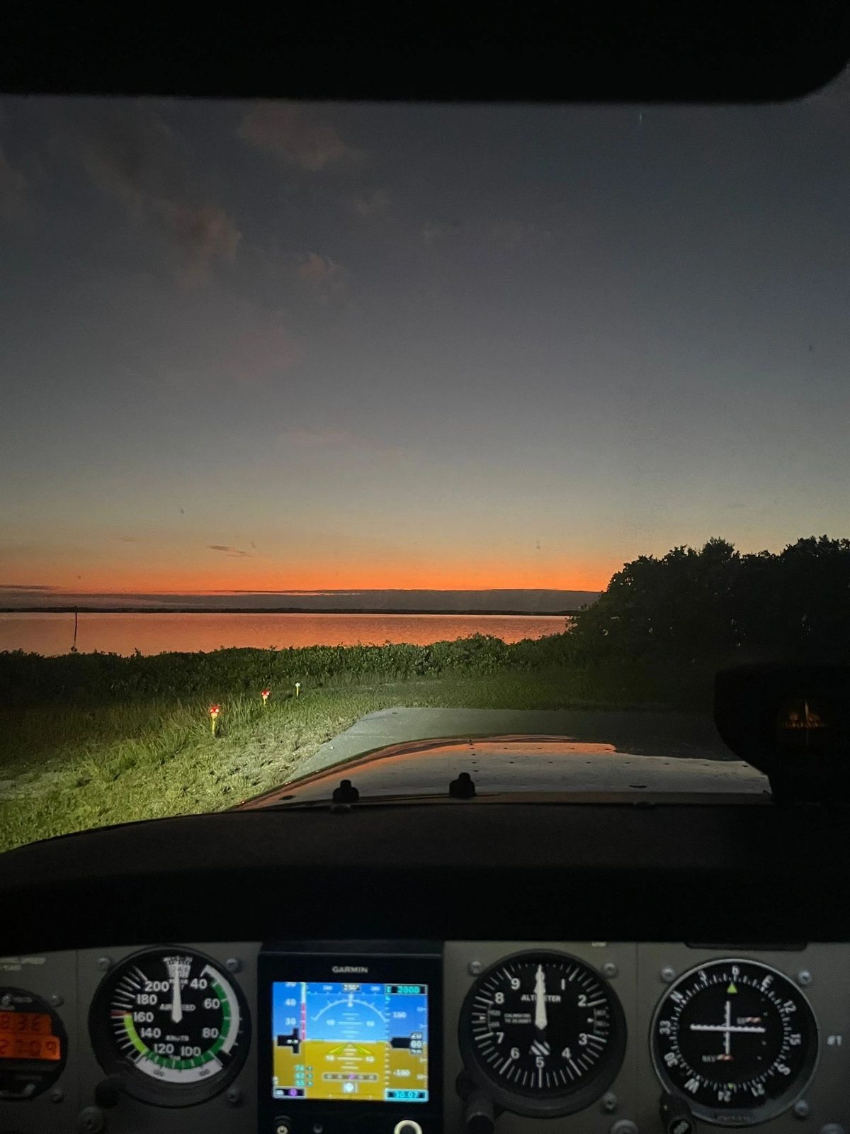 Dusk over the airfield from the cockpit, with the instrument panel and glass display lit