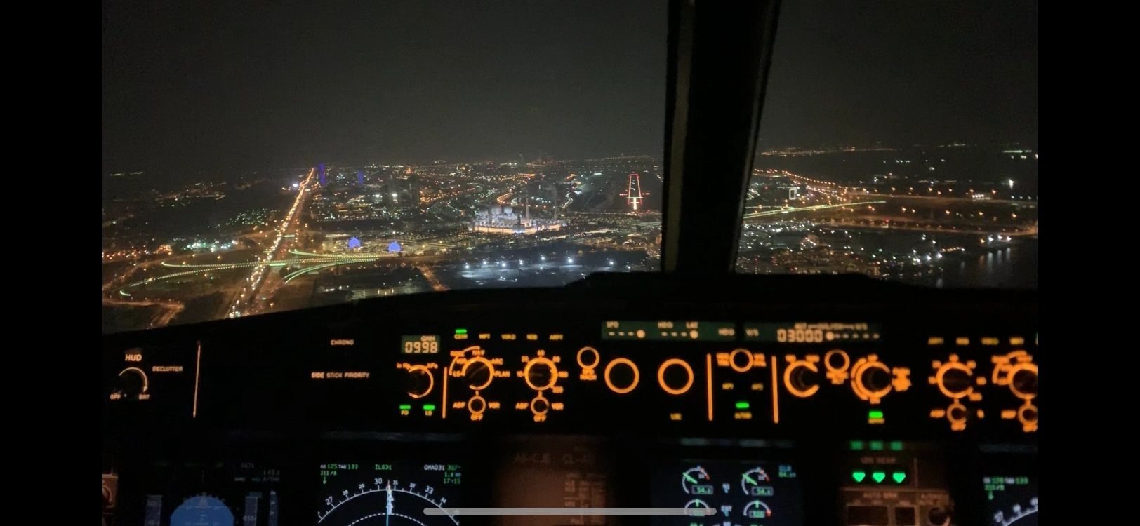 Night approach towards a lit city, seen from an illuminated flight deck