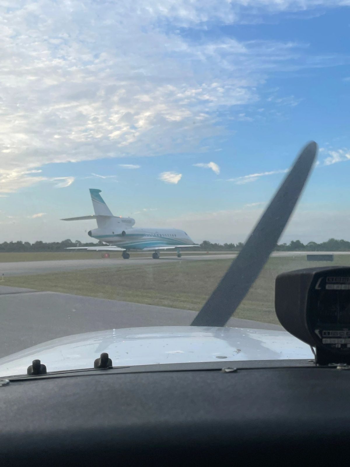 A business jet on the taxiway, seen over the cowling of a training aircraft